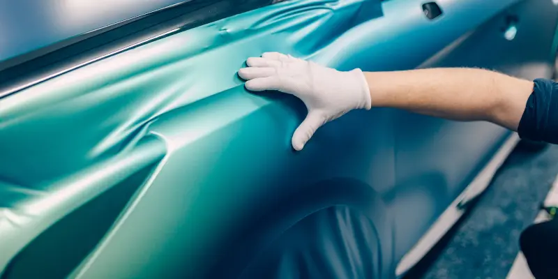 Car wrapping specialist putting vinyl foil or film on car. Selective focus.